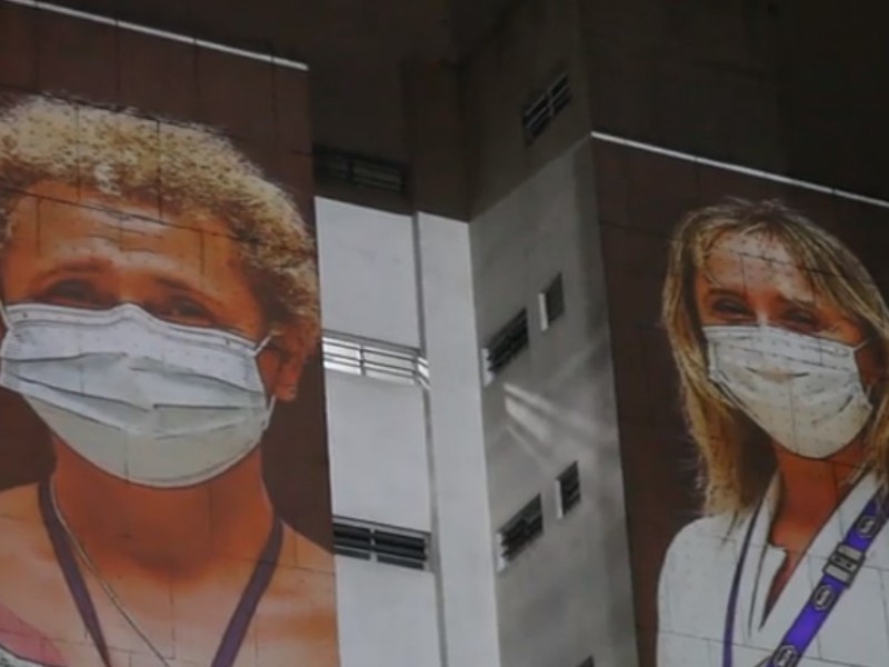 Duas mulheres profissionais da saúde têm suas fotos projetadas na lateral de um prédio